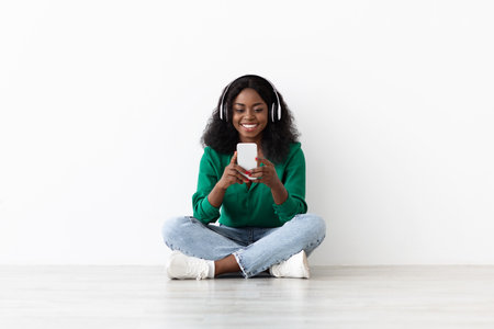 Young Woman Enjoying Music With Headphones While Sitting on Floor in Bright Indoor Spaceの写真素材