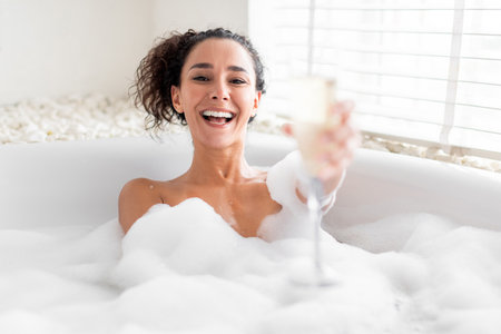 Enjoying a Relaxing Bubble Bath With Champagne While Smiling in a Warmly Lit Bathroomの写真素材