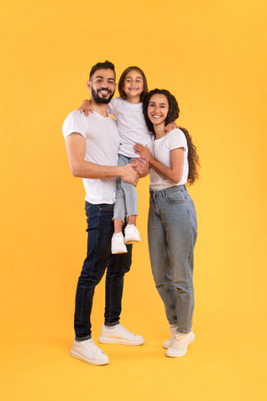 Family Smiles Together Against Bright Yellow Backdrop During Casual Indoor Photoshootの写真素材