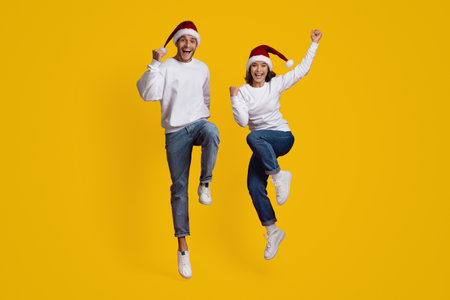 Excited Young Couple Celebrating Christmas With Santa Hats Against a Bright Yellow Backgroundの写真素材