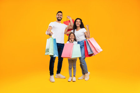 Happy Family Celebrating a Shopping Day With Colorful Bags on a Bright Yellow Backgroundの写真素材