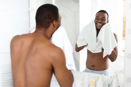 Man Enjoying Morning Routine While Drying His Face in Bathroom Mirrorの写真素材