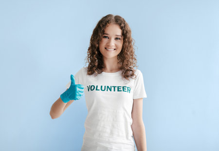 Young Woman Volunteering and Showing Thumbs up While Wearing Gloves in a Light Blue Settingの写真素材