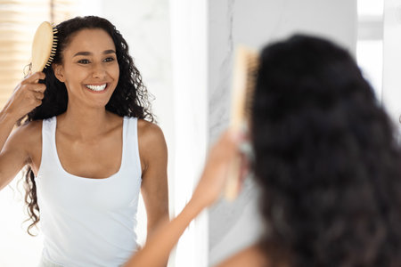 Woman Brushing Her Curly Hair in Front of a Mirror in a Bright Bathroom During the Morningの写真素材