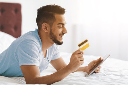 Young Man Shopping Online With a Credit Card While Lying on Bedの写真素材