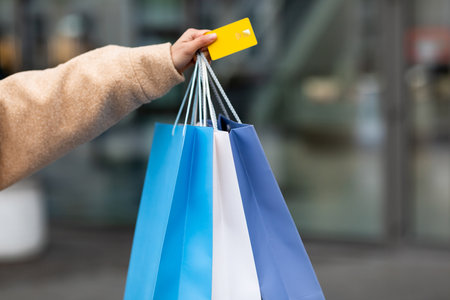 Shopping Bags Held by a Person Displaying a Credit Card in a Busy Urban Area During Daytimeの写真素材