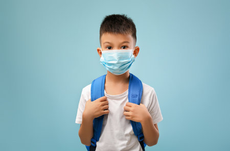 Young Boy With a Backpack Wearing a Face Mask in a Blue Background Prepares for School During Health Precautionsの写真素材