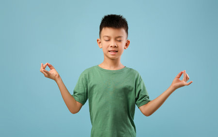 Young Boy Practicing Mindfulness and Meditation With a Calm Expression Against a Blue Backgroundの写真素材