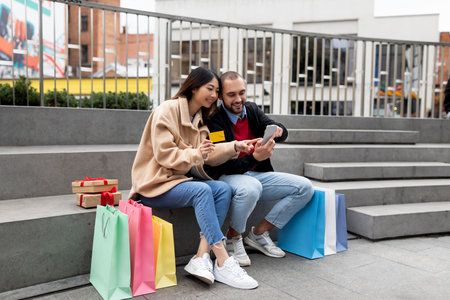 Couple Enjoying a Shopping Break While Looking at Their Phone in a City Squareの写真素材