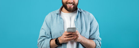 Man Smiles While Using Smartphone in Studio Against Blue Backgroundの写真素材