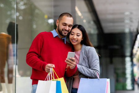 Couple Enjoying Shopping Together While Checking Their Smartphone Outside a Store in a Busy Urban Settingの写真素材
