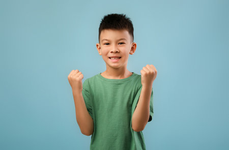 Young Boy Celebrating Success With Enthusiasm in a Bright Blue Background During Daytimeの写真素材