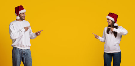 Friends in Christmas Hats Smiling and Pointing at Each Other on a Bright Yellow Backgroundの写真素材