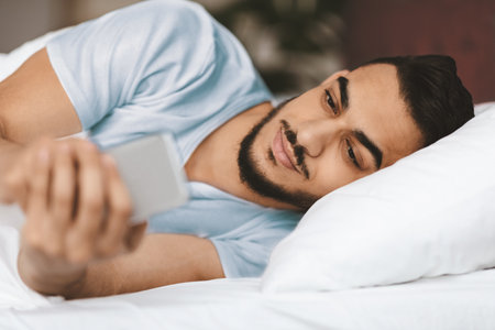 Man Relaxing in Bed While Using Smartphone During Morning Hoursの写真素材