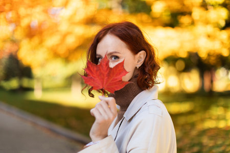 Woman Holding a Red Maple Leaf in an Autumn Parkの写真素材