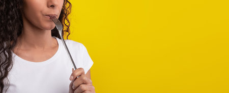 Woman With Curly Hair Holding a Fork Against a Bright Yellow Backgroundの写真素材