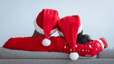 Couple in Christmas Sweaters and Hats Enjoying Holiday Moments Together on the Couchの写真素材