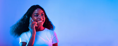 Young Woman Smiling While Talking on the Phone in Vibrant Lightingの写真素材