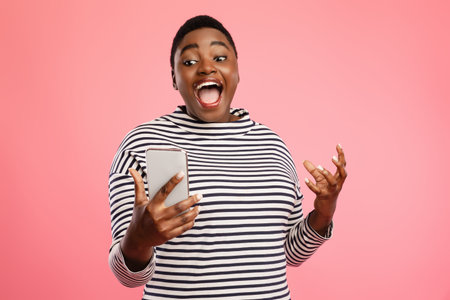 Woman Expressing Joy While Looking at Her Smartphone Against a Pink Backgroundの写真素材