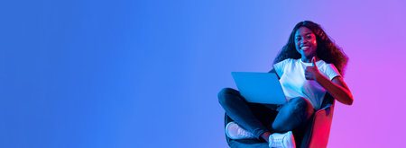 Young Woman Sits Comfortably With Laptop Giving Thumbs up in Vibrant Colored Settingの写真素材