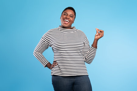 Happy Woman in Striped Shirt Smiling Against a Blue Background While Striking a Fun Pose