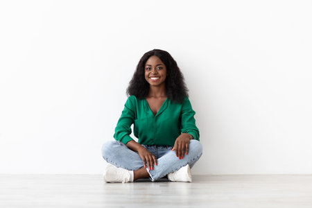 Young Woman Sitting on the Floor With a Smile in a Bright, Minimalistic Room During the Dayの写真素材