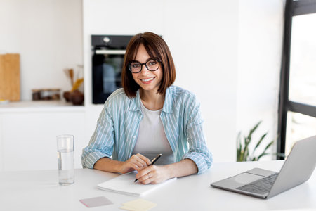 Young Woman Working at a Modern Desk During the Day With a Laptop and Notepadの写真素材
