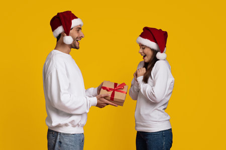 Couple Exchanges Gift During Holiday Celebration Against Bright Yellow Backgroundの写真素材