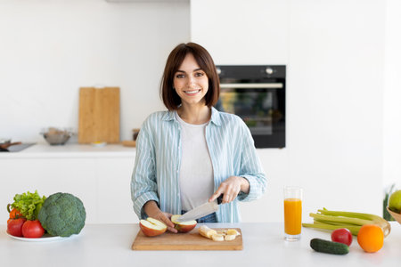 Woman Chopping Fruits and Vegetables in a Bright Kitchen While Preparing a Healthy Mealの写真素材