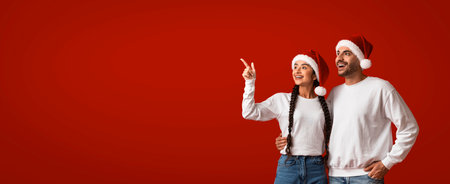 Holiday Celebration With Cheerful Couple Wearing Santa Hats Against Red Backdropの写真素材