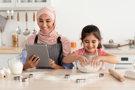 Mother and Daughter Enjoy Baking Together With a Tablet in a Bright Kitchenの写真素材