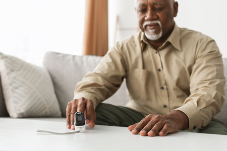 Senior Man Checking His Health With a Pulse Oximeter at Home While Sitting on a Comfortable Couch in the Living Roomの写真素材