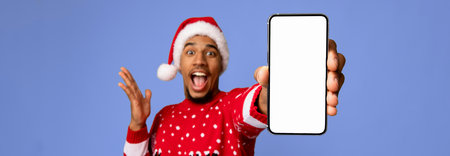 Excited Man in Christmas Sweater Shows off Smartphone in Festive Settingの写真素材