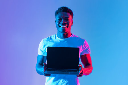 Young Man Smiles While Holding Laptop Against Colorful Backgroundの写真素材