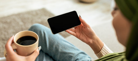 Enjoying Coffee While Using Smartphone in Cozy Living Room Spaceの写真素材