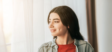 Young Woman Enjoying a Quiet Moment by the Window in Soft Natural Lightの写真素材