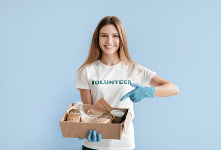Smiling Volunteer Holding a Food Donation Box With a Blue Backgroundの写真素材