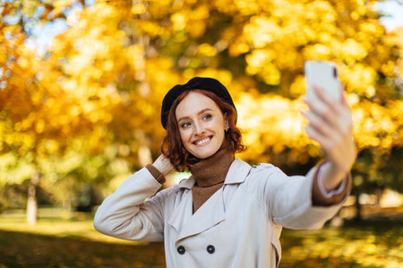 Young Woman Taking a Selfie in a Park Surrounded by Bright Autumn Leaves During a Sunny Day