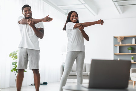 Young black couple doing arm stretch exercise watching online tutorial