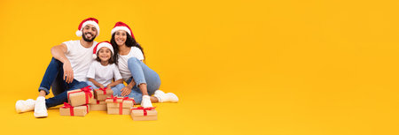 Happy Family Celebrating Christmas in Festive Hats With Gifts on Yellow Backgroundの写真素材