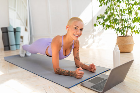Workout for keep fit during covid-19 quarantine. Happy young lady in sportswear doing plank on mat in front of laptopの写真素材