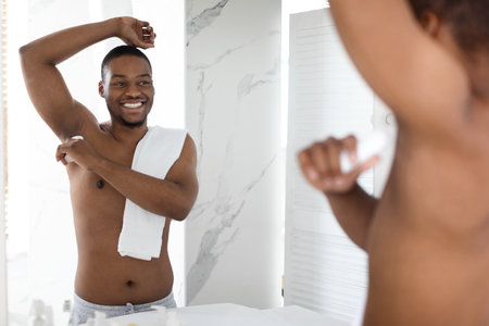 Man Smiling While Applying Deodorant in Modern Bathroom Mirror During Morning Routineの写真素材