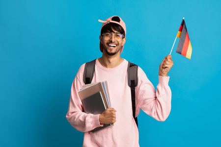 Student Celebrating Cultural Pride With a Small German Flag in a Cheerful Pose Against a Bright Blue...