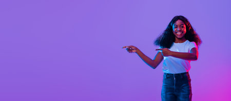 Young Woman Points Towards Colorful Background in Studio Setting With Vibrant Lightingの写真素材