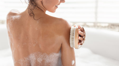 Woman Using a Body Brush While Enjoying a Relaxing Moment in a Bubble Bath at Home During the...