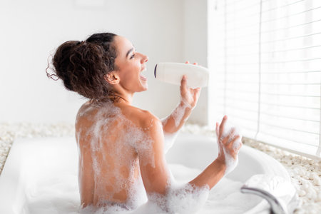 Woman Enjoying Bubble Bath With a Bottle in Hand While Laughing in a Bright Bathroom