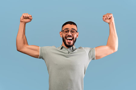 Man Celebrating With Raised Arms and a Joyful Expression in Front of a Blue Background