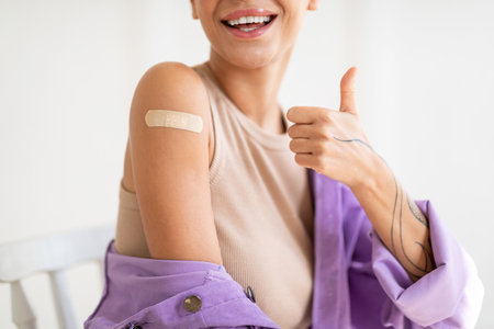 Successful covid-19 vaccination. Closeup view of lady gesturing thumb up and showing arm with adhesive bandageの写真素材