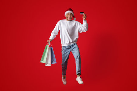 Joyful Shopper Celebrating Christmas With Colorful Bags and Credit Card Against Bright Red Backdropの写真素材