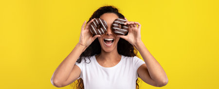 Joyful Woman Playfully Holding Donuts in Front of Her Face Against Bright Yellow Background